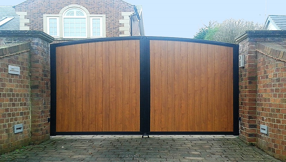 Driveway gates with curved top and aluminium panels designed to look like wood.